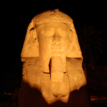 Statue of head of Ramses lighted at night against black background.