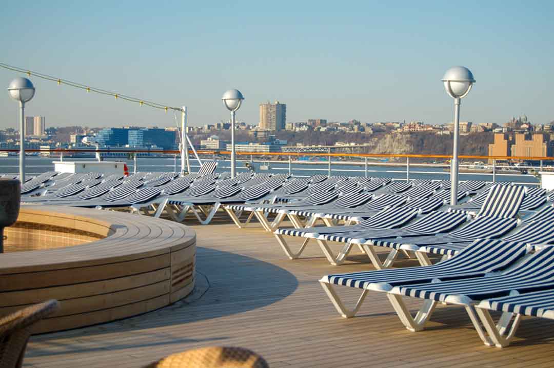 Holland America Line cruise ship sun deck with empty white lounge chairs covered with blue and white stripped cushions