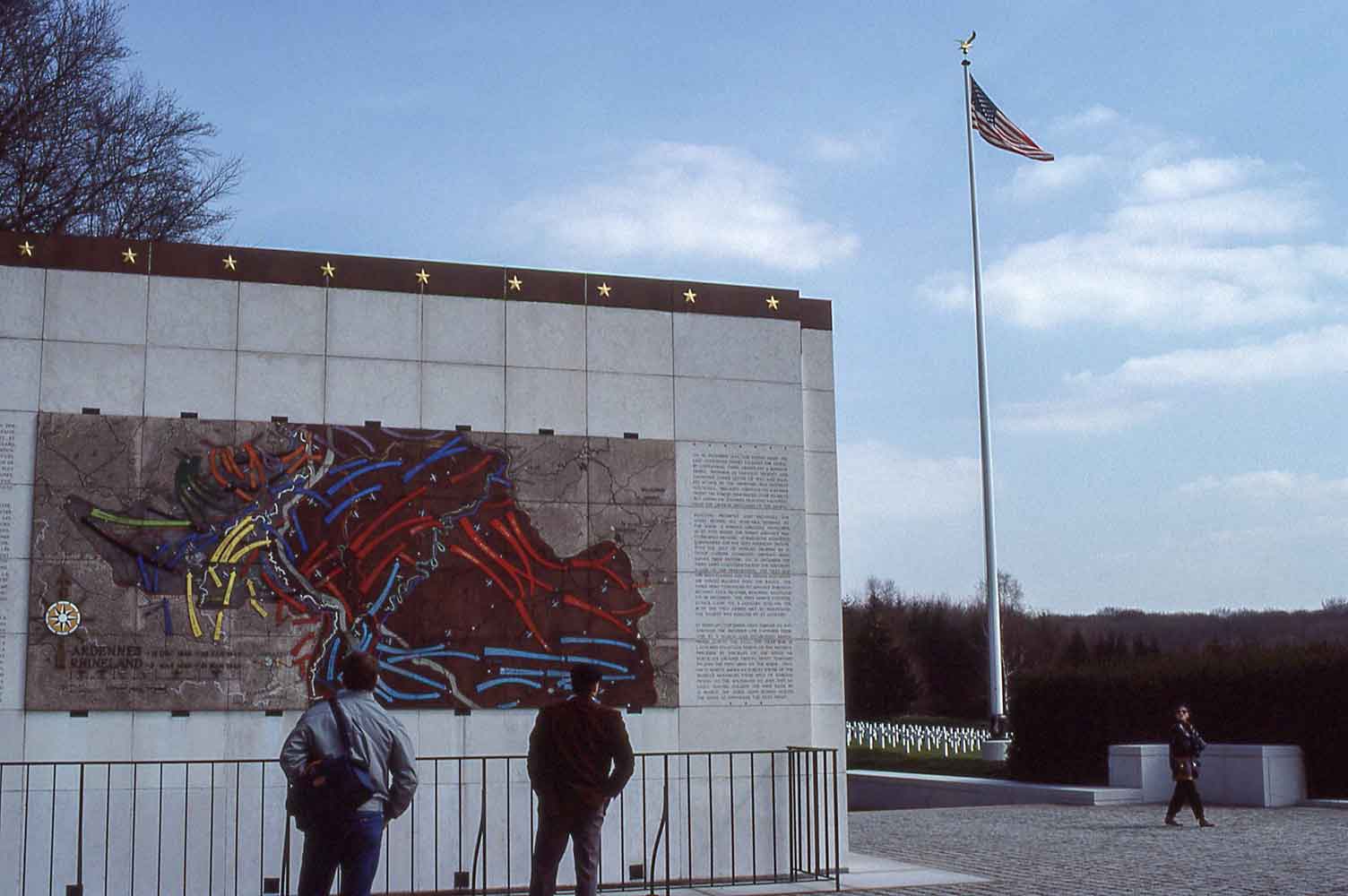 Diorama detailing the Battle of the Bulge and the American flag outstretched in the breeze with the crosses of the cemetery in the background