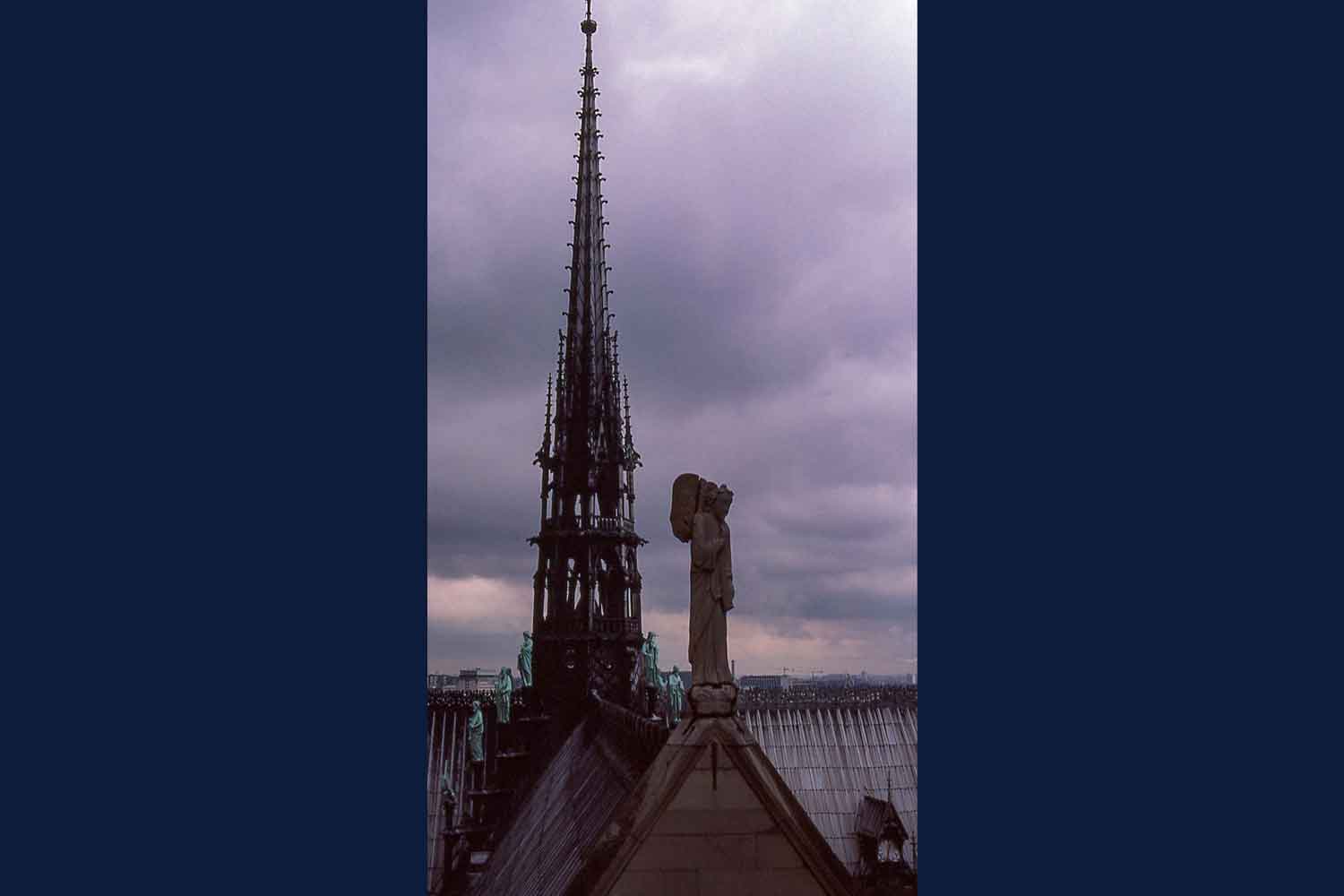 Roof top showing a tall thin spire and some of the statues of the 12 Apostles and 4 Evangelists along the roof peak along with an angel watching over the church.