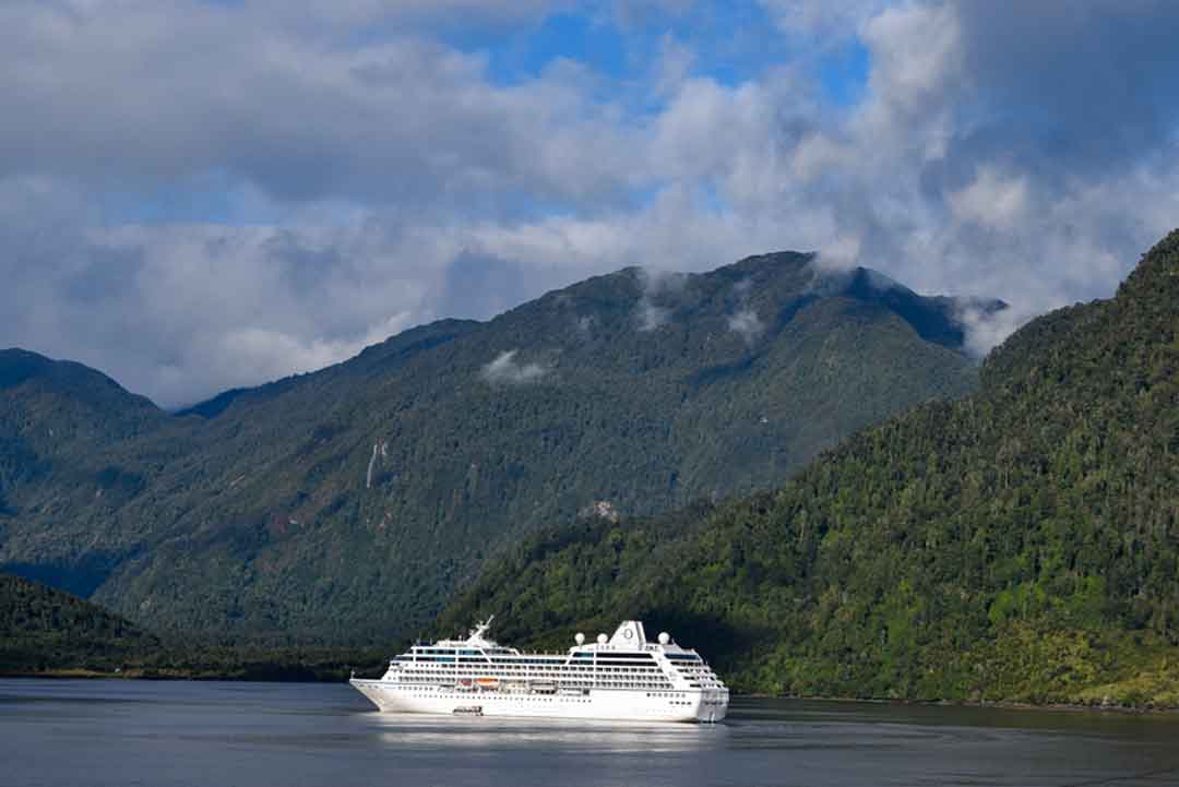 white cruise ship in water surrounded by green mountains demonstrating the difference in cruise lines
