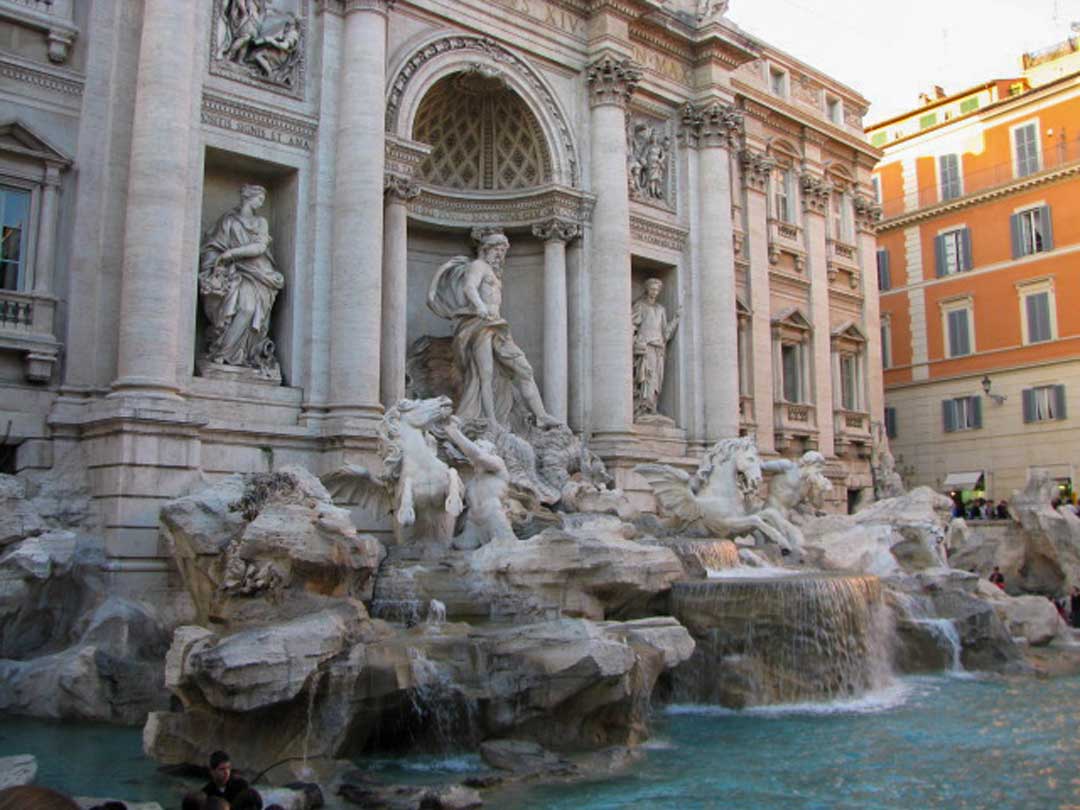 Large white ornately decorated marble fountain with water running over the rocks into the bottom of the fountain. Trevi Fountain, Rome, Italy.