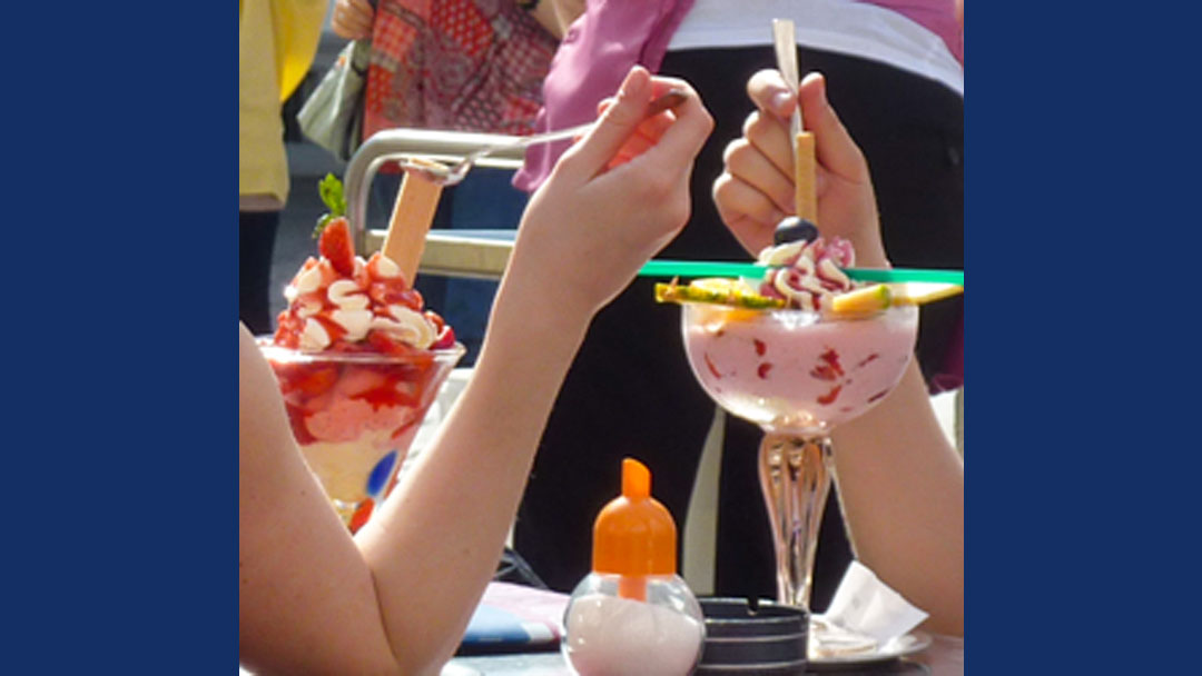 close up of two very large, long stemmed glasses, filled with ice cream and various toppings.