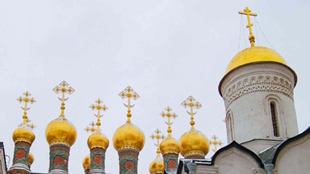 Multiple gold domes on top of smaller spires. Spires covered with red and green decorations. One larger gold dome on top of rounded tower.