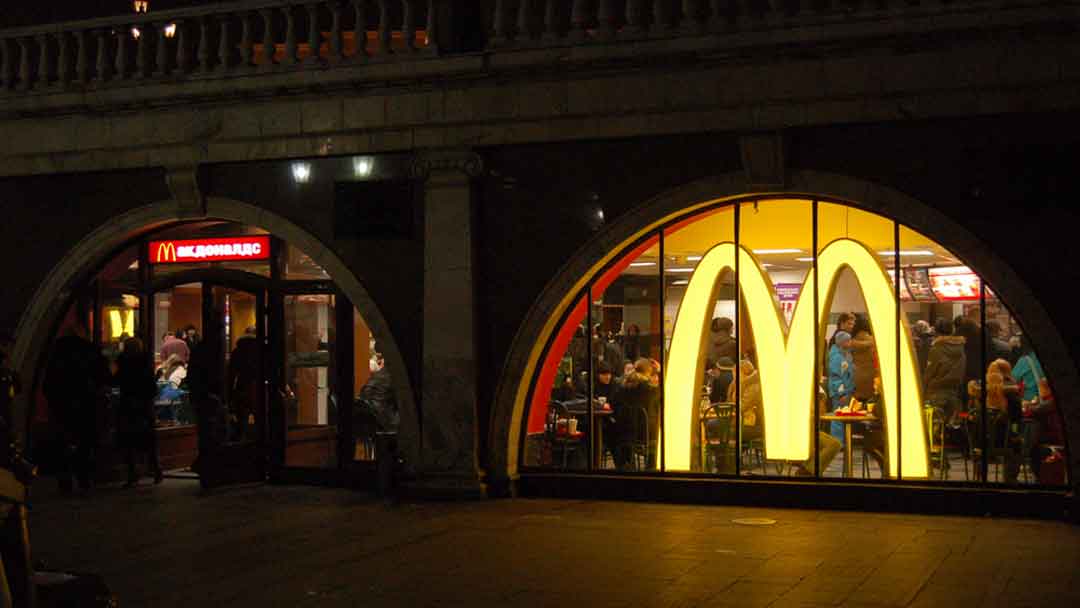 Picture of two arched windows one with a door. Over the door is a large rectangular sign with McDonald's written in cyrillic. In the other window is a large M, McDonald's golden arches. Inside the store is filled with people.