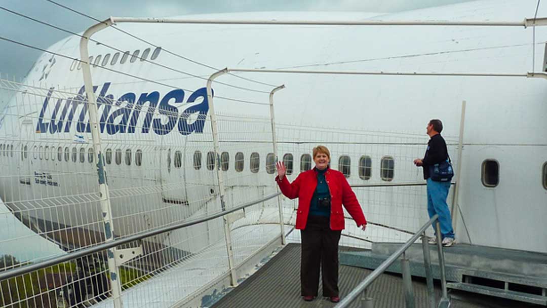 Woman standing on platform over the wing of a large aircraft (Boeing 747) which is on a structure holding it about 30 -40 feet above the ground