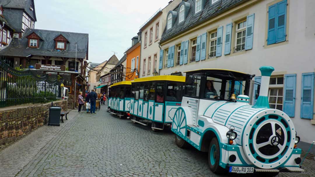 White tram decorated to look like a small train on a cobblestone road