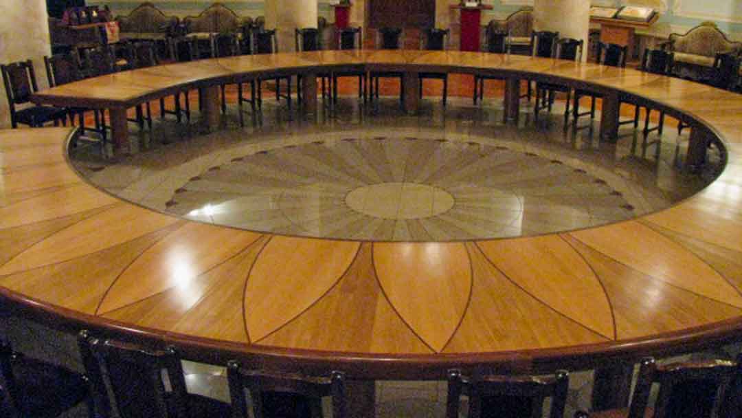 Large circular wood table with and opening and the center removed so that someone could walk from person to person seated at the table. Table is wood with wood inlay