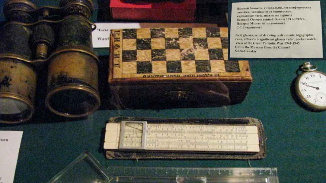 Collection of items used during Stalinist period: well worn binoculars, worn portable chess set, slide rule, pocket watch all set in a display