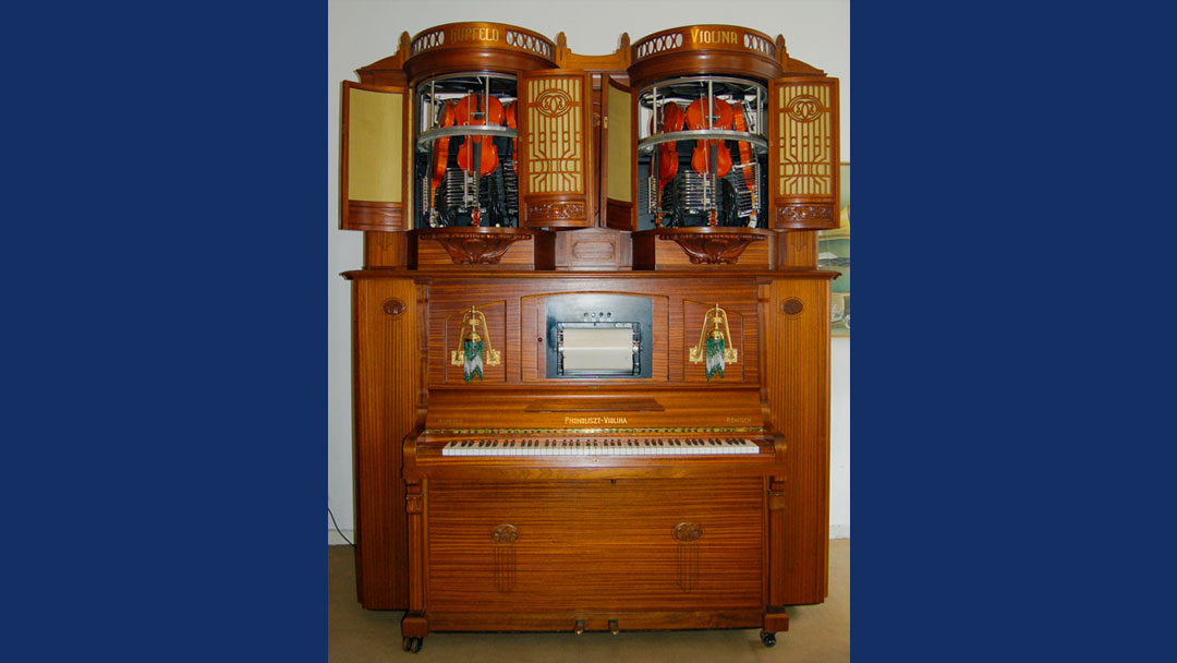 what looks like a brown wood upright piano, but at top are two cabinets each with four violins in them. This is a mechanical violin player.