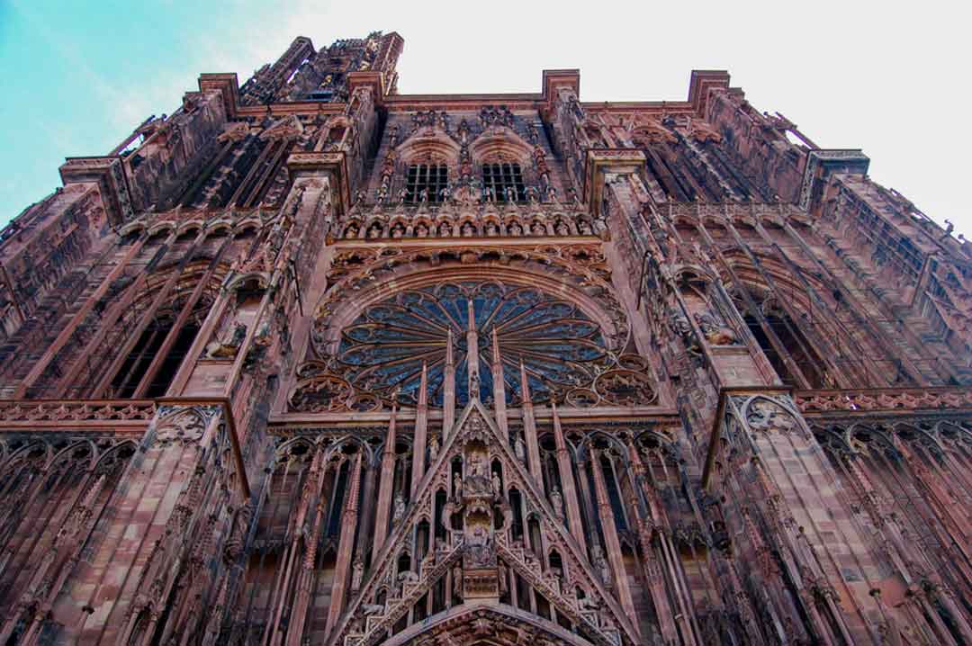 Looking upward to top of a very tall gothic cathedral reddish orange in color, elaborately decorated