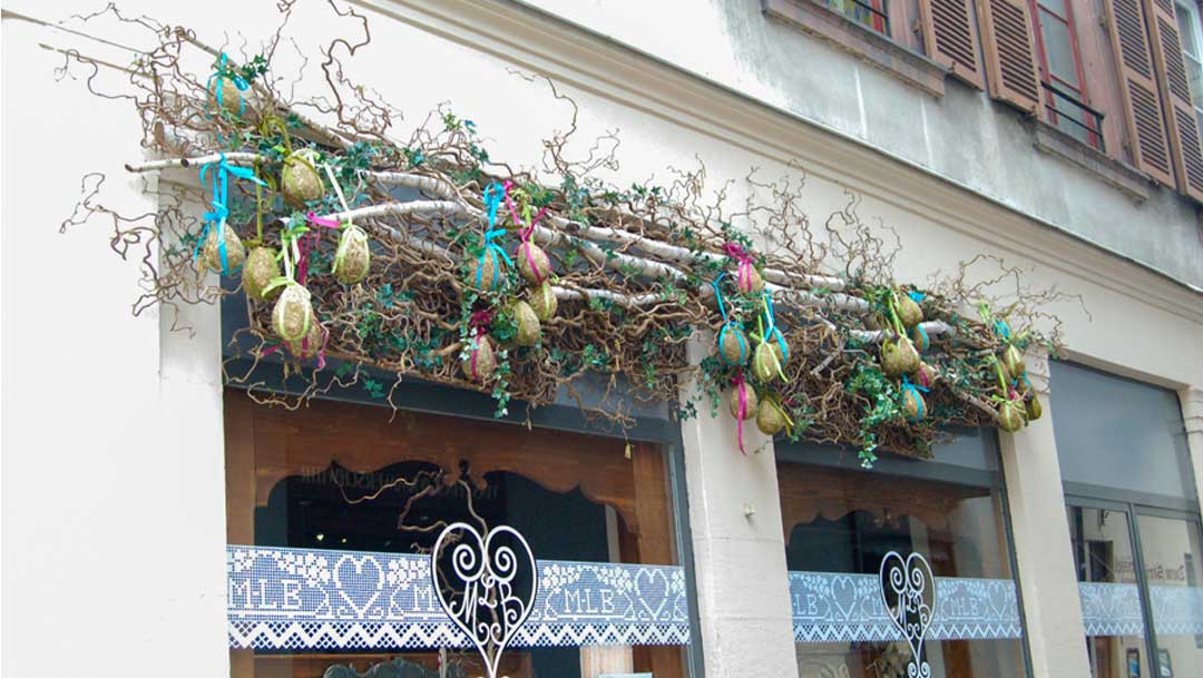 shop window with bough made of several sticks tied together with vines and decorated with colorful Easter eggs hanging from ribbons