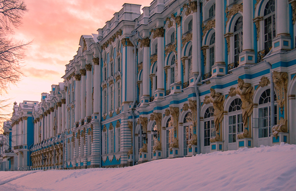 Building painted blue with whit pillars and white windows. Trim on pillars and windows are gold leaf. Sun is setting casting a pink glow on the clouds, and snow on the ground.