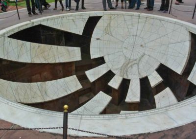 Large white marble concave structure in the ground with parts of the marble cut out. Etchings on the marble.