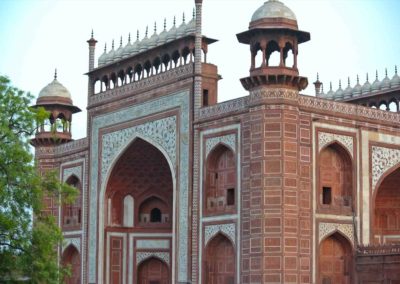 Gate of the Taj Mahal made of red sandstone topped with two large domes and numerous smaller domes.