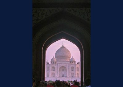 Taj Mahal seen through a gateway which frames the entire building. The Taj Mahal is tinged slightly pink from the rising sun.