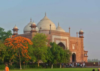 View of the red sandstone guest house within the Taj Mahal complex, in front are several variety of trees, one with orange colored blooms.