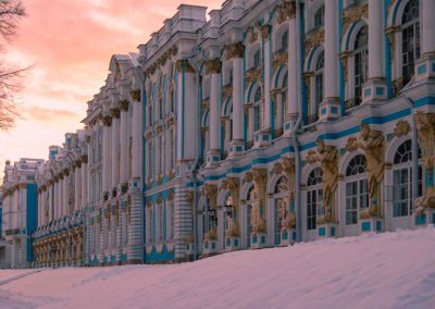 Building painted blue with whit pillars and white windows. Trim on pillars and windows are gold leaf. Sun is setting casting a pink glow on the clouds, and snow on the ground.