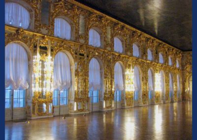 Very large room with numerous sets of windowed double doors, topped by arched windows reaching to the ceiling. The space between the windows and doors is covered in elaborate gold decorations. The floor is wood inlay. The ceiling is painted with a scene, and is very dark. There are sheer curtains over the windows and doors.