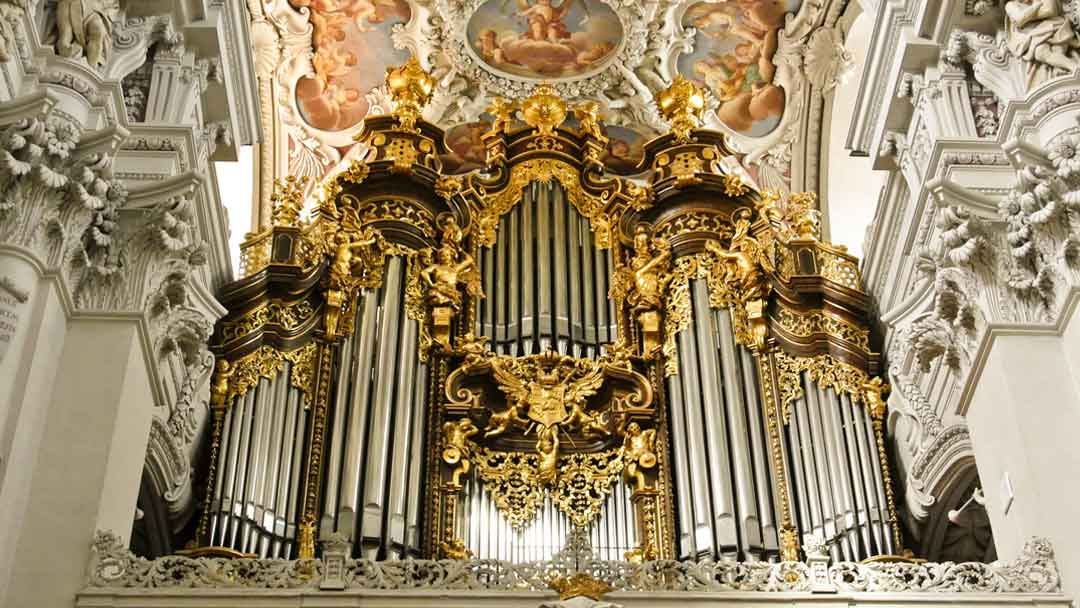 numerous pipes of an organ. Silver with gold trim set within a white ornately decorated church