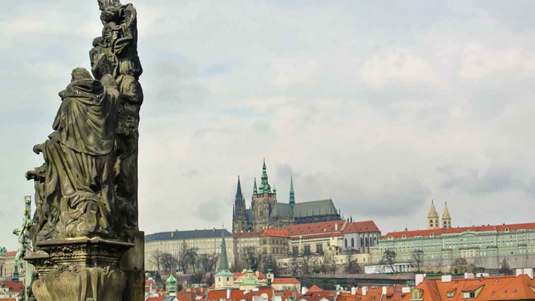 view of Prague Castle up on a hilltop in the distance with a statue of the Charles Bridge in the foreground