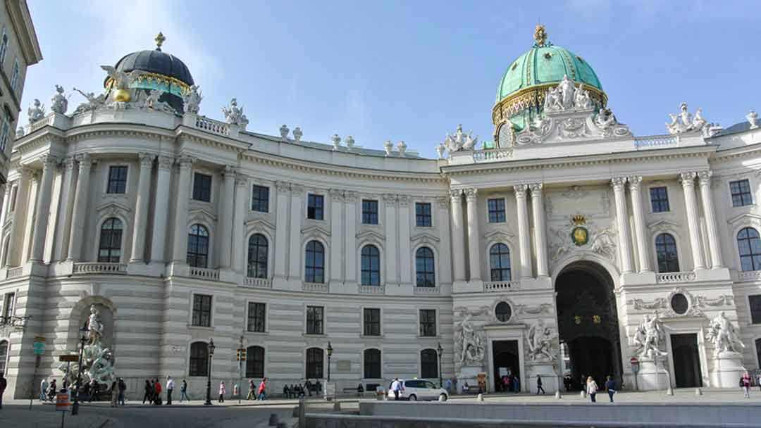 Elaborate, large white marble building with domes covered in green copper.