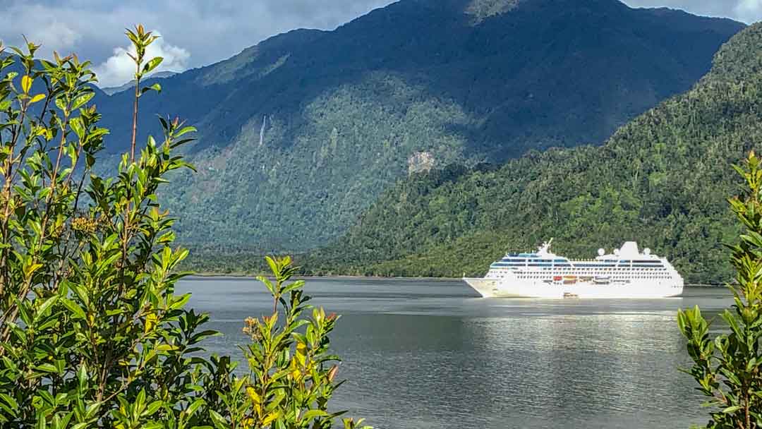 Cruise ship in bay with green mountains surrounding it