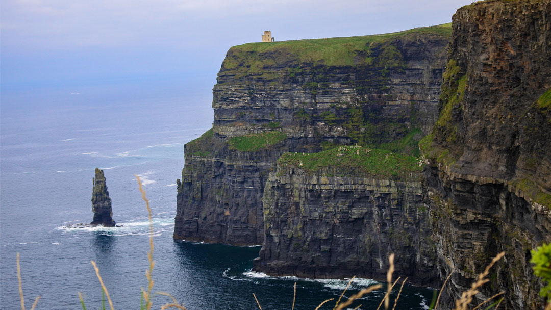 Tall dark cliffs topped with green grass overlooking the ocean. Small lookout tour at the top of the cliffs.