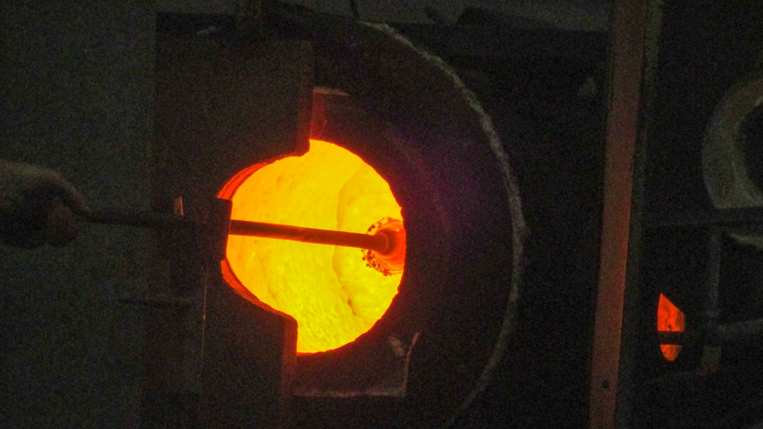 Glowing furnace with glass blowers tube and ball of glass on the end.