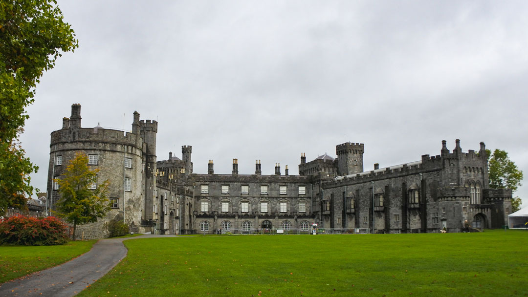 A large gray stone walled castle with green grass in the foreground.