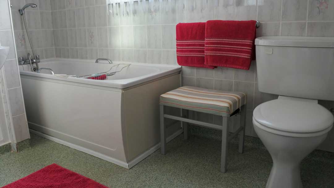 Large bathroom showing tub, toilet, bench and towels