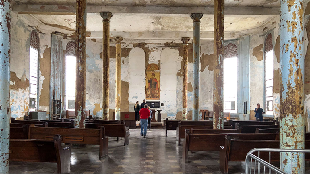 large room with numerous pillars. Paint and stucco are peeling off walls and pillars. In center is a lecturn area with a large icon photo behind. Area was used as a chapel within the Ohio State Reformatory.