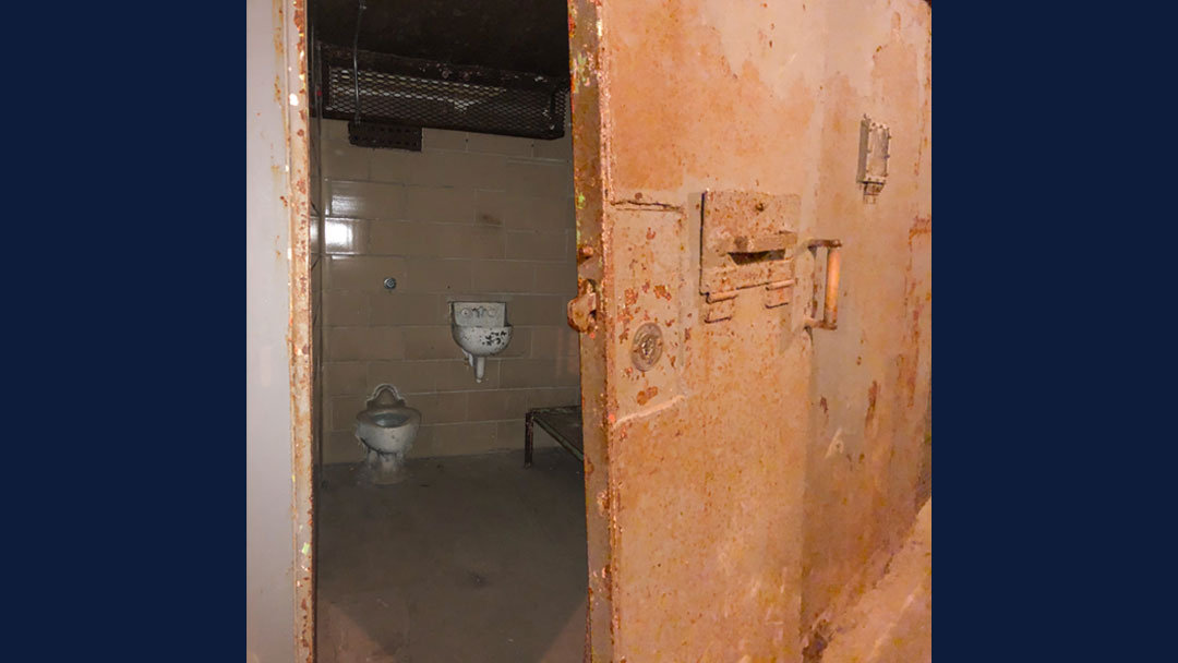 Heavy rusted metal door ajar showing interior of solitary confinement cell of Ohio State Reformatory